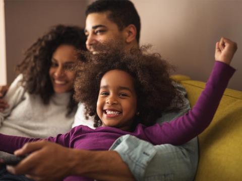 Family on a couch, smiling, with little girl cheering